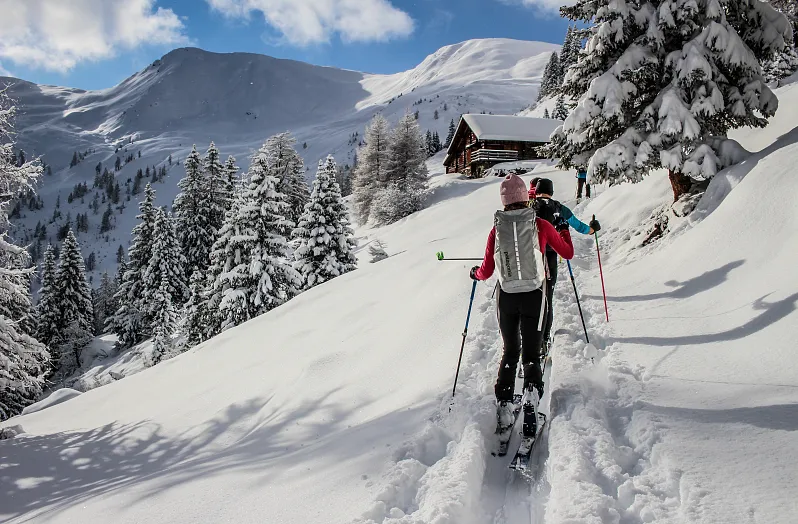 Zwei Skitourengeher wandern auf verschneitem Pfad bergauf, umgeben von schneebedeckten Tannen und Bergen im Großarltal.