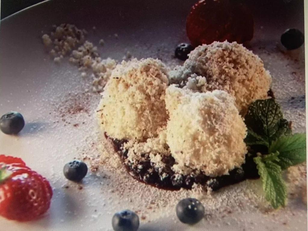 Drei Kugeln Vanilleeis mit Keksbröseln, umgeben von Heidelbeeren, Erdbeere und Minzblatt auf weißem Teller
