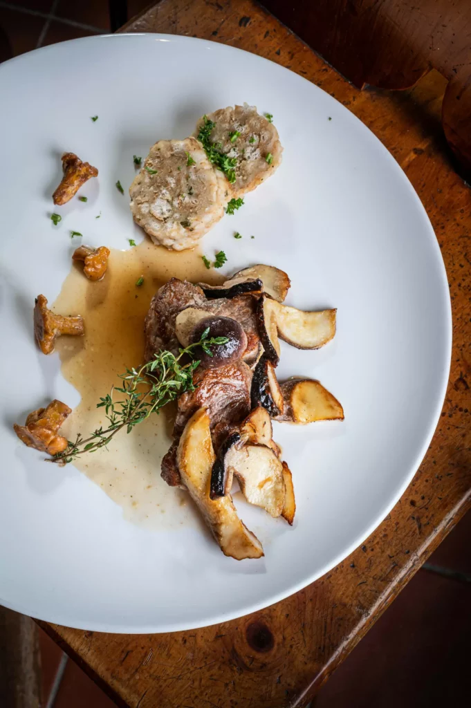 Gebratenes Fleisch mit Pilzen, zwei Semmelknödeln und Sauce auf weißem Teller auf rustikalem Holztisch