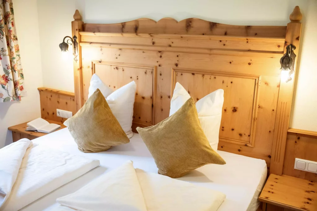 Gemütliches Hotelzimmer mit Holzbett, weißen Bettdecken und zwei braunen Kissen im Naturhotel Hüttenwirt Großarl