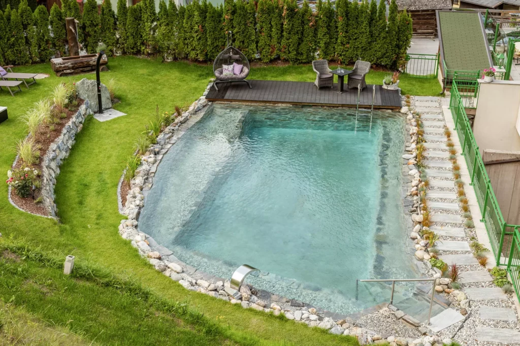 Außenpool mit klarem Wasser, Liegestühlen, Sitzbereich und grüner Gartenanlage im Naturhotel Hüttenwirt Großarl