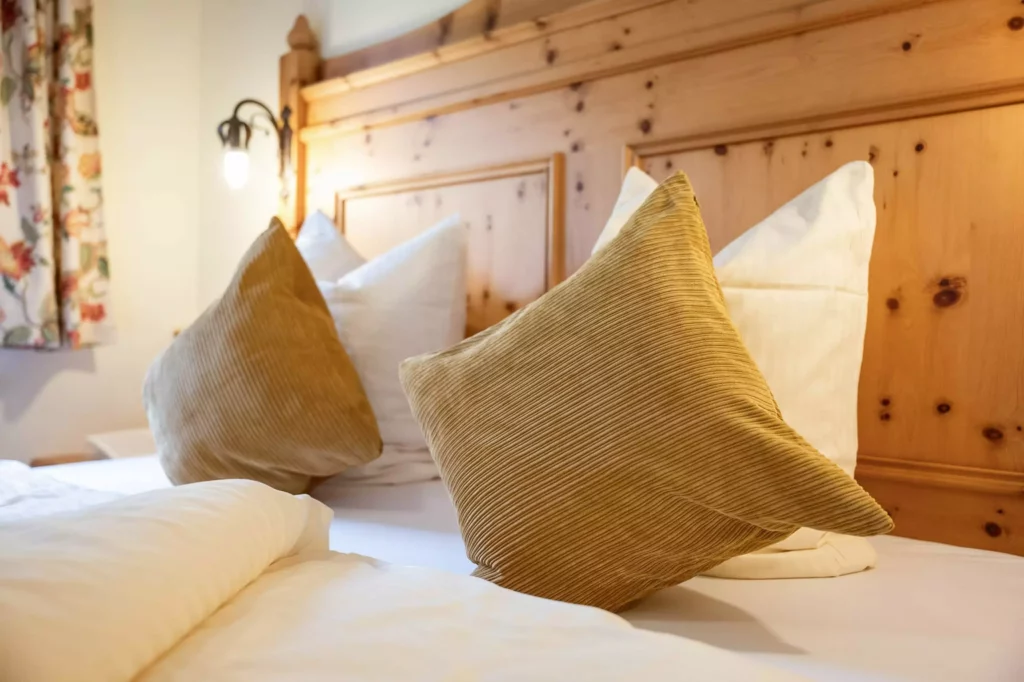 Gemütliches Hotelbett mit weißen und braunen Kissen vor einem Holz-Kopfteil im Naturhotel Hüttenwirt Großarl
