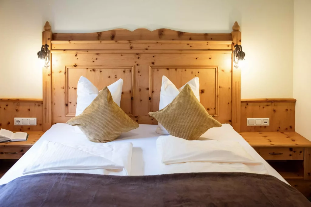 Doppelbett mit Holzkopfteil, zwei weißen und zwei braunen Kissen, Nachttischen mit Lampen und Steckdosen im Naturhotel