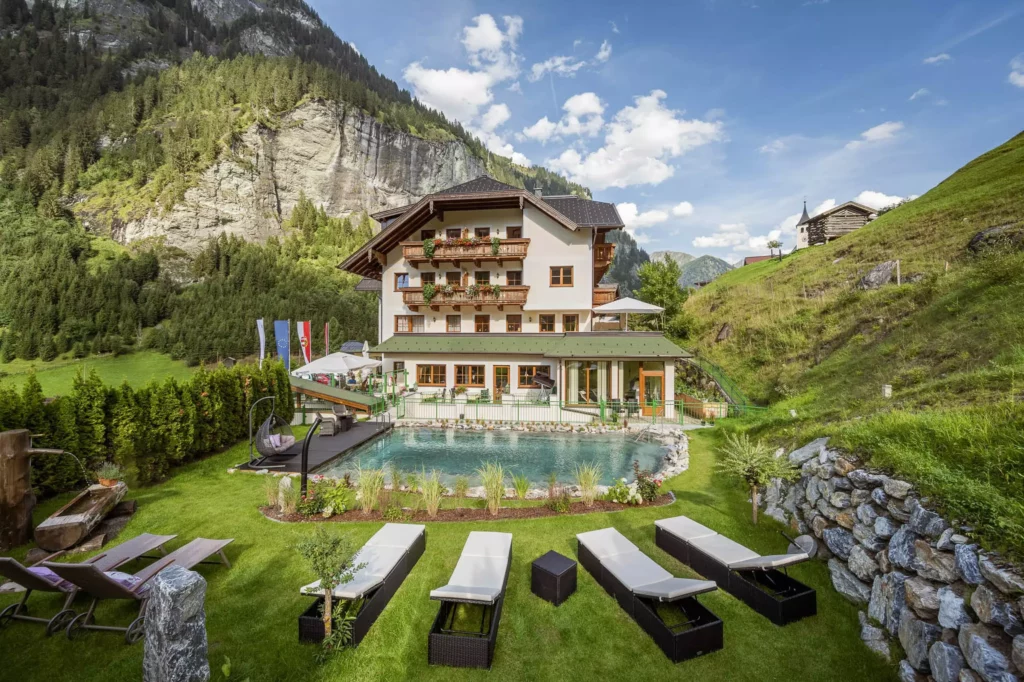 Naturhotel Hüttenwirt in Großarl mit Liegen am Naturpool, umgeben von Bergen und grüner Landschaft im Großarltal