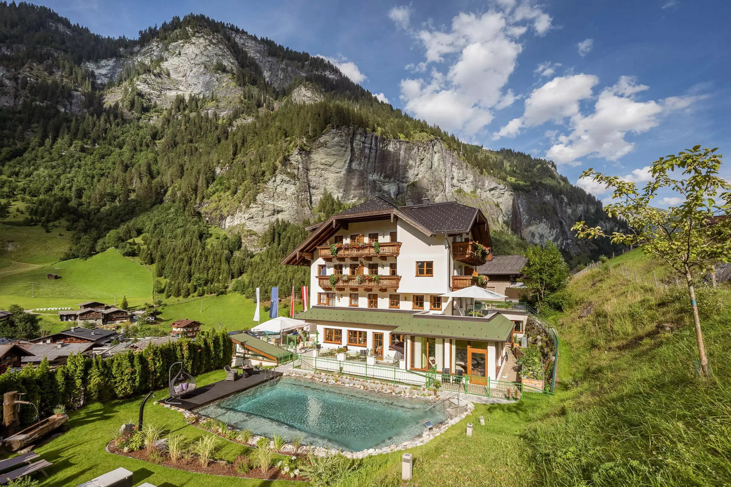 Naturhotel Hüttenwirt in Großarl mit Außenpool vor Bergkulisse und grüner Landschaft im Großarltal Hohen Tauern