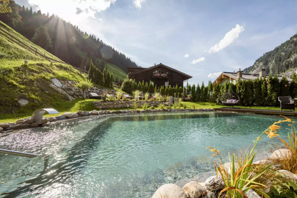 Natürlicher Schwimmteich mit klarem Wasser vor einer Holzhütte und Bergen im Großarltal bei Sonnenschein