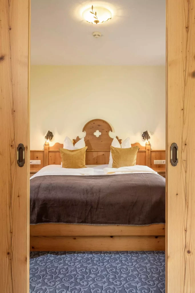 Gemütliches Hotelzimmer mit Holzbett, brauner Decke, gelben Kissen und Teppich, Naturhotel Hüttenwirt Großarl Hohen Tauern