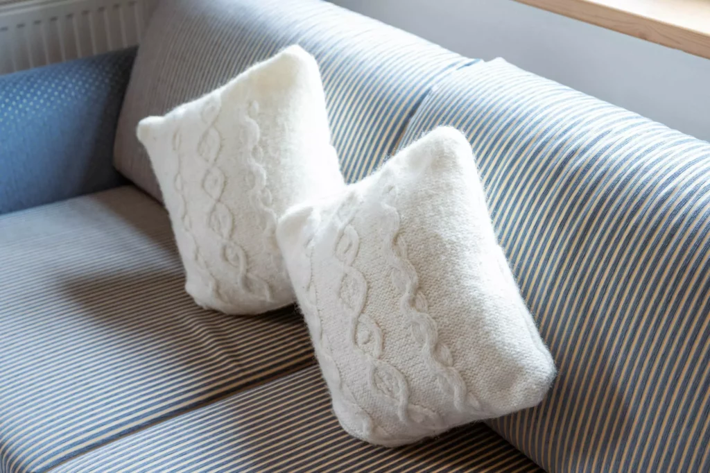 Zwei weiße, gestrickte Kissen auf einem blau-weiß gestreiften Sofa im Naturhotel Hüttenwirt Großarl