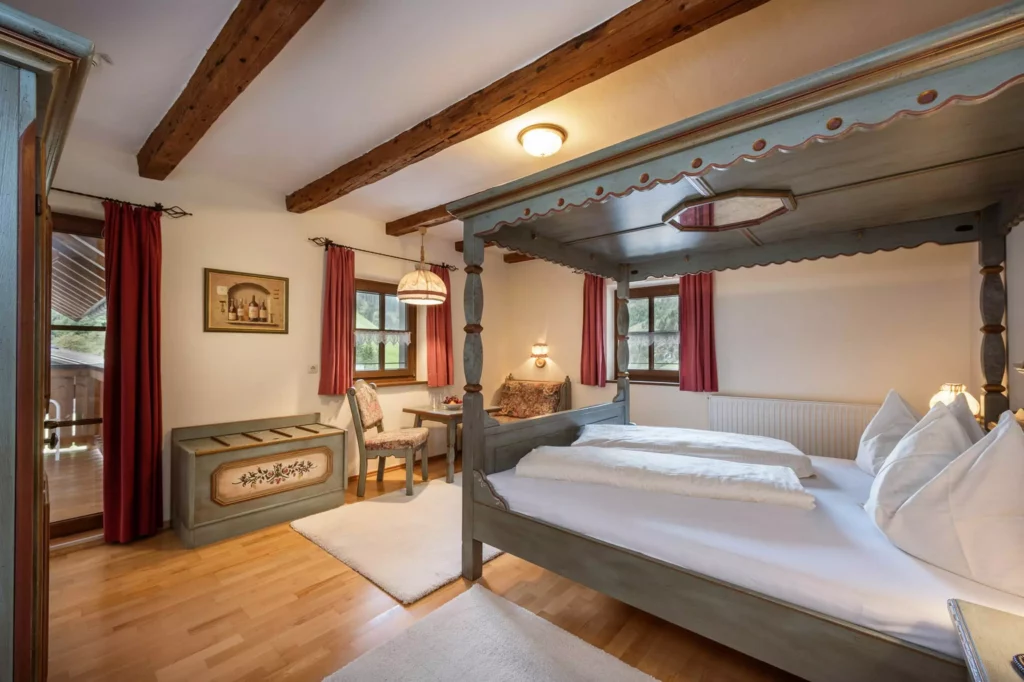 Gemütliches Hotelzimmer mit Himmelbett, Holzbalken, roten Vorhängen und Sitzbereich im Naturhotel Hüttenwirt Großarl Hohen
