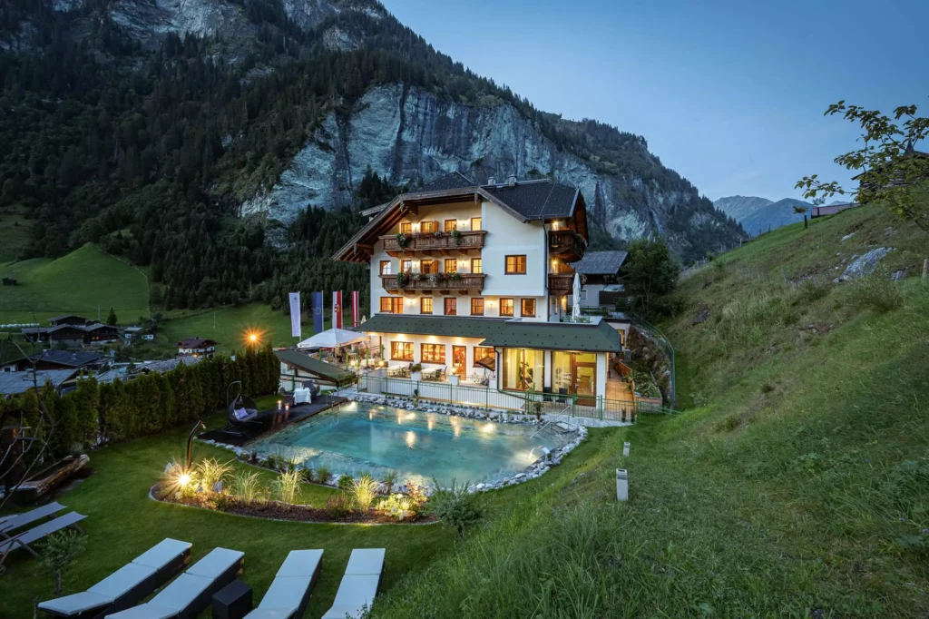 Naturhotel Hüttenwirt in Großarl mit beleuchtetem Außenpool und Liegen vor Bergkulisse am Abend im Großarltal Hohen Tauern