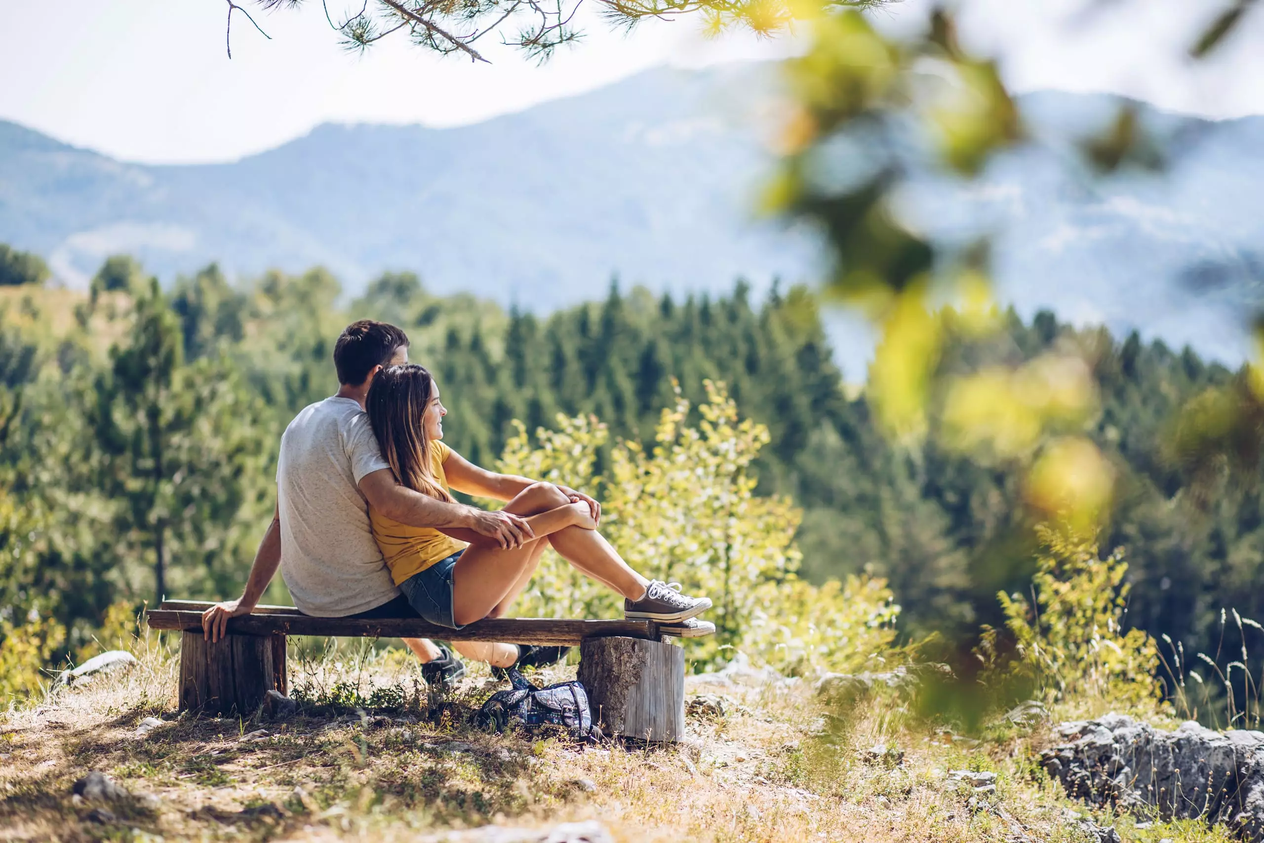Paar sitzt auf einer Holzbank in der Natur mit Blick auf bewaldete Berge im Großarltal bei Sonnenschein