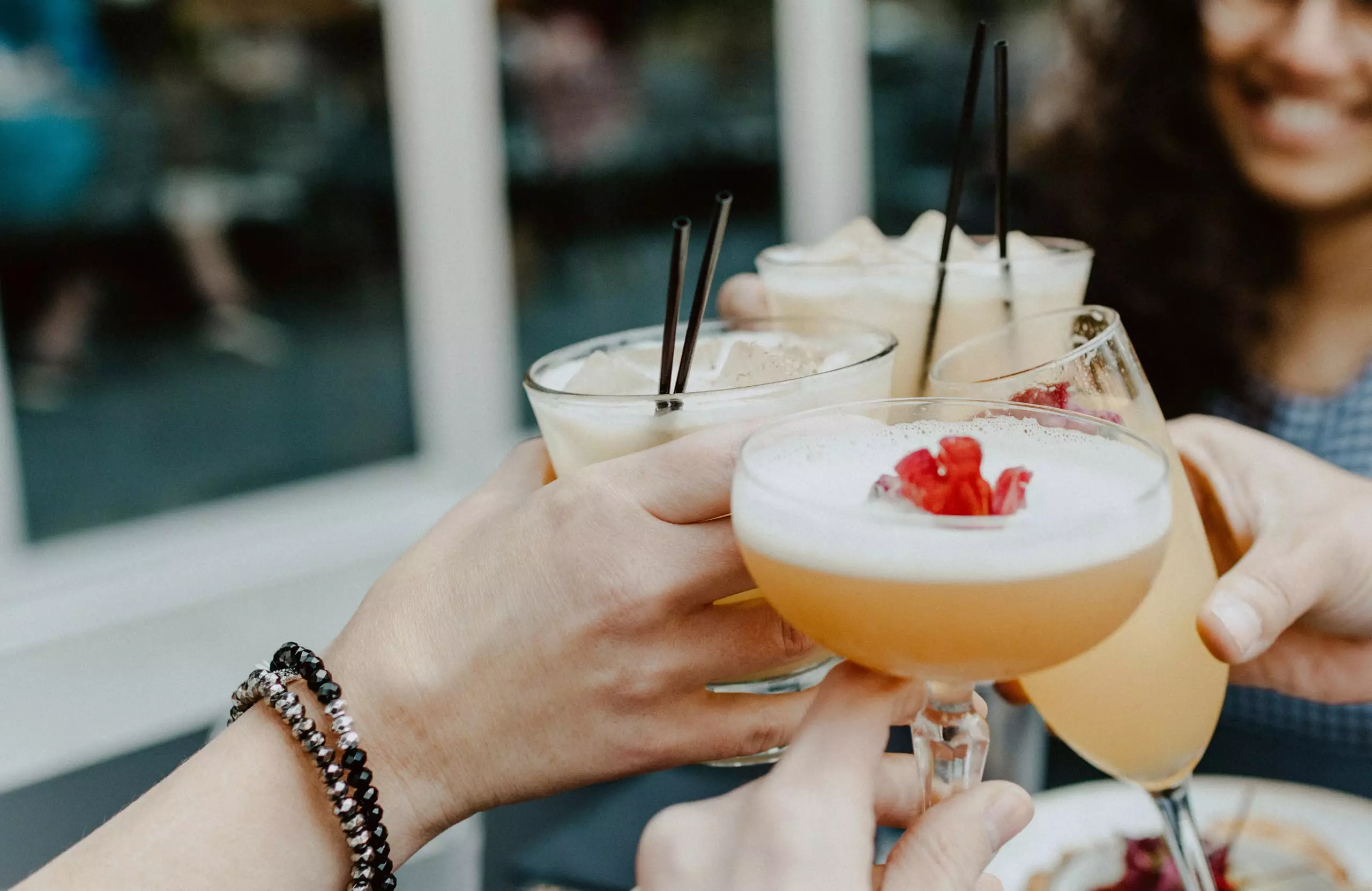 Mehrere Hände stoßen mit verschiedenen Cocktails in Gläsern bei einem geselligen Treffen an, Naturhotel Hüttenwirt Großarl